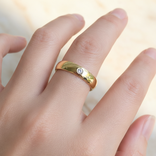 A sleek, half-round shaped gold band with a single, prominently displayed white diamond set in the center.