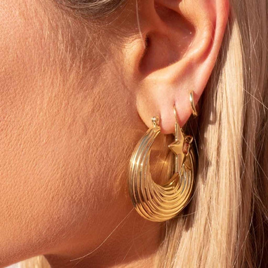 A pair of gold-plated brass hoop earrings with a textured pattern, displayed against a grey background.