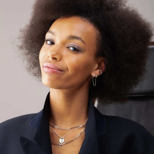 A pair of gold chain linked mismatched huggie hoop earrings with one hoop featuring a row of small crystals.