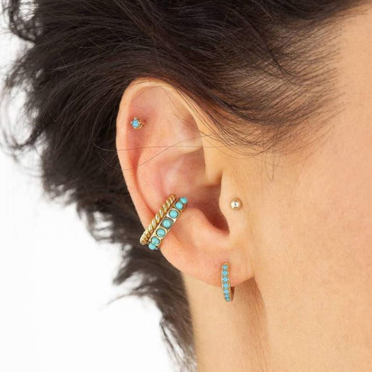 A set of gold and turquoise earrings, including different styles such as huggie and studs, displayed against a neutral background.