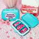 Blue pill organizer with 'lactose intolerant girls' text, strawberry milk container, and decorative items on a checkered background.