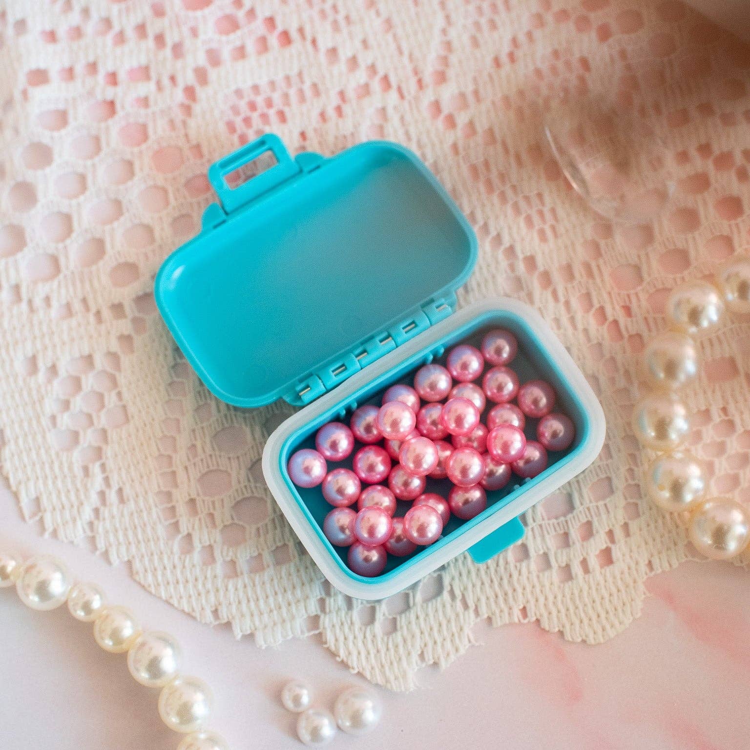 Blue container filled with pink pearls on a lace background