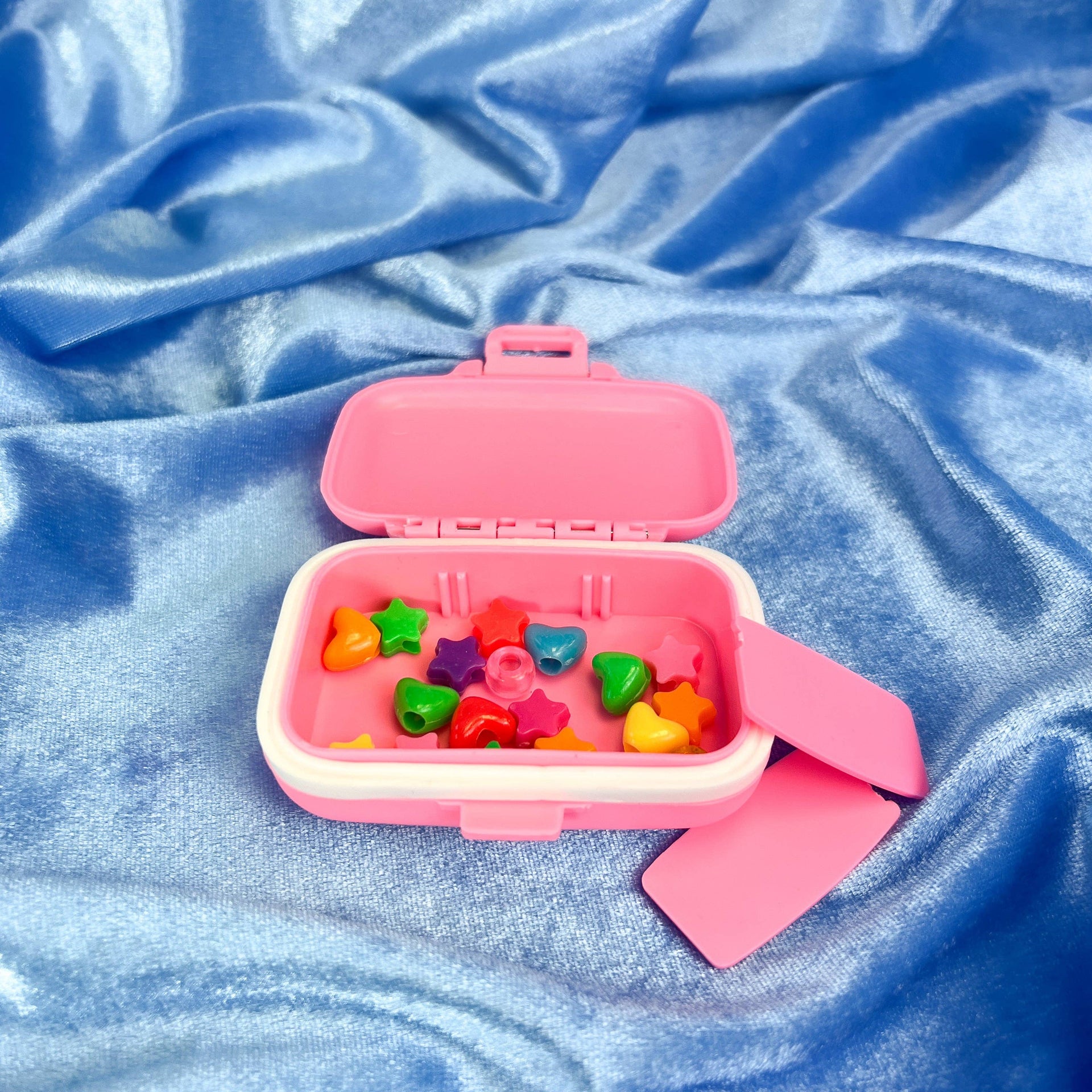 Pink pillbox with colourful heart-shaped beads on a blue textured fabric background