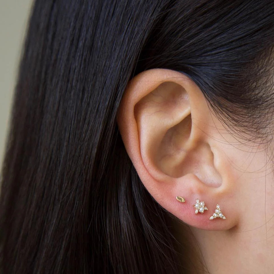 Close-up of an ear wearing gold and silver earrings with dark hair.