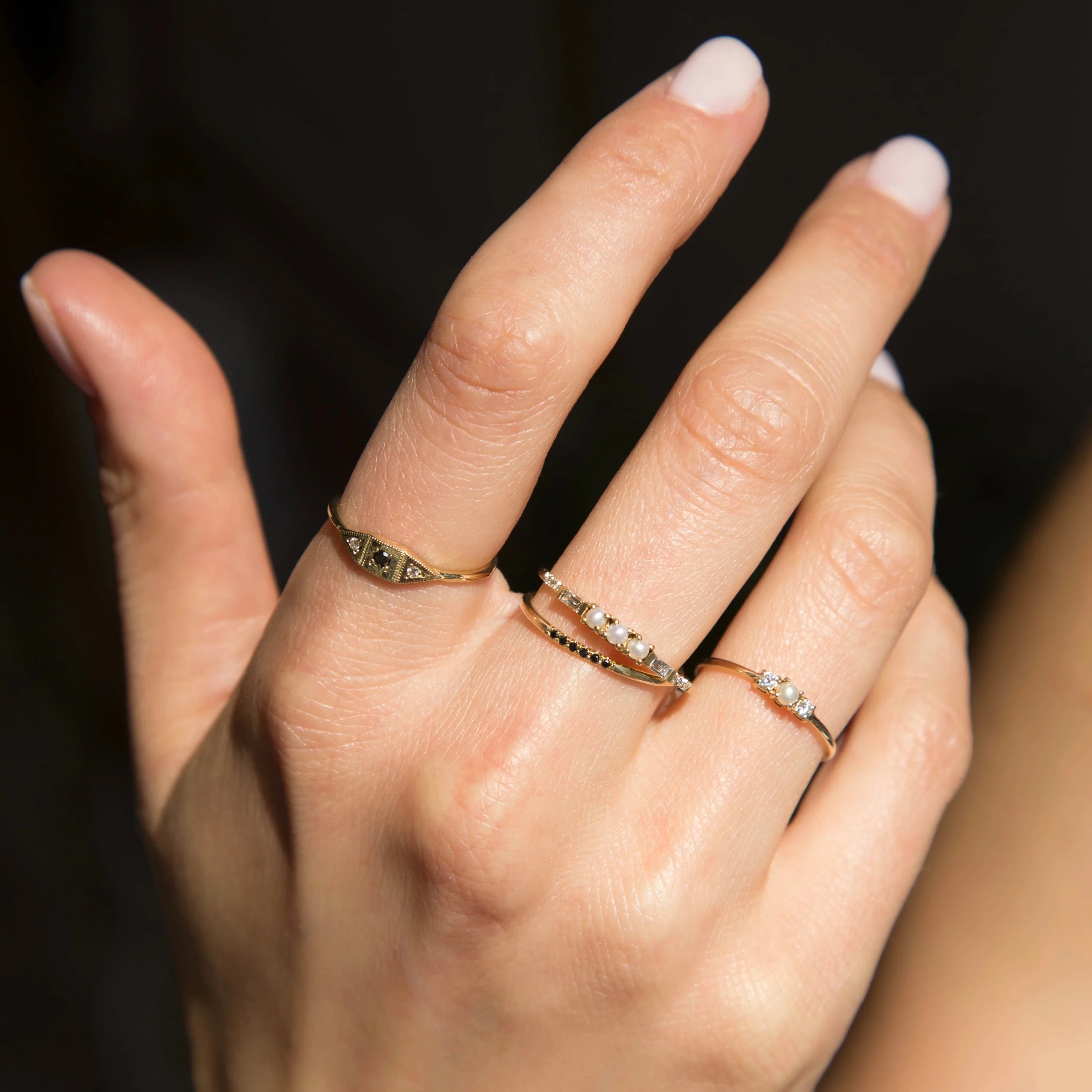 A mixture of dainty black diamond, white diamond and pearl rings by Jennie Kwon on a model's hand.