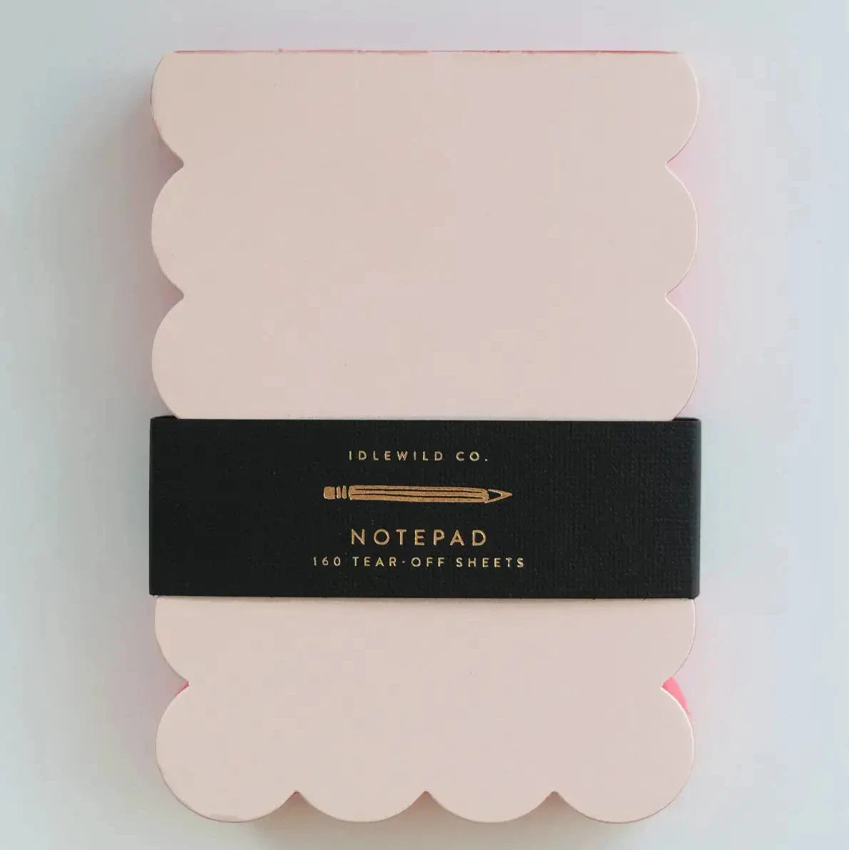 A scalloped, peach-colored notepad with a black, contrast-colored edge and the Idlewild Co. brand name on the spine.