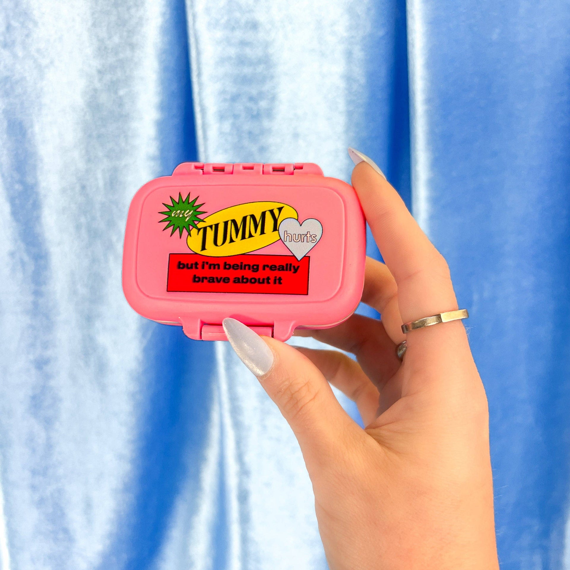 Pink container with a humorous label held by a hand against a blue curtain background