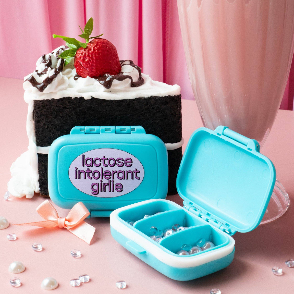 Blue pill case with 'lactose intolerant girl' text next to a cake and milkshake on a pink background