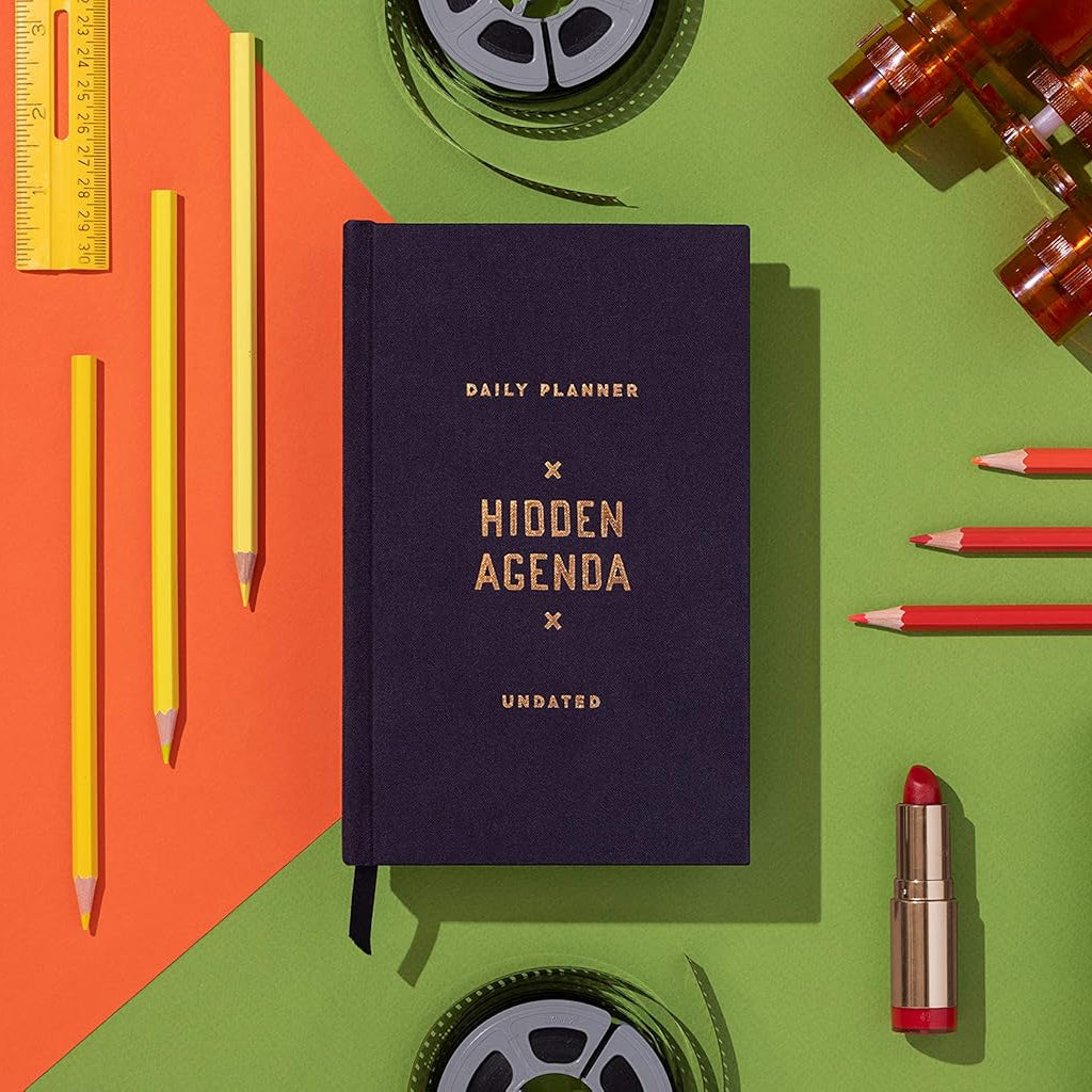 Planner book titled 'Hidden Agenda' surrounded by stationery items on a colorful background