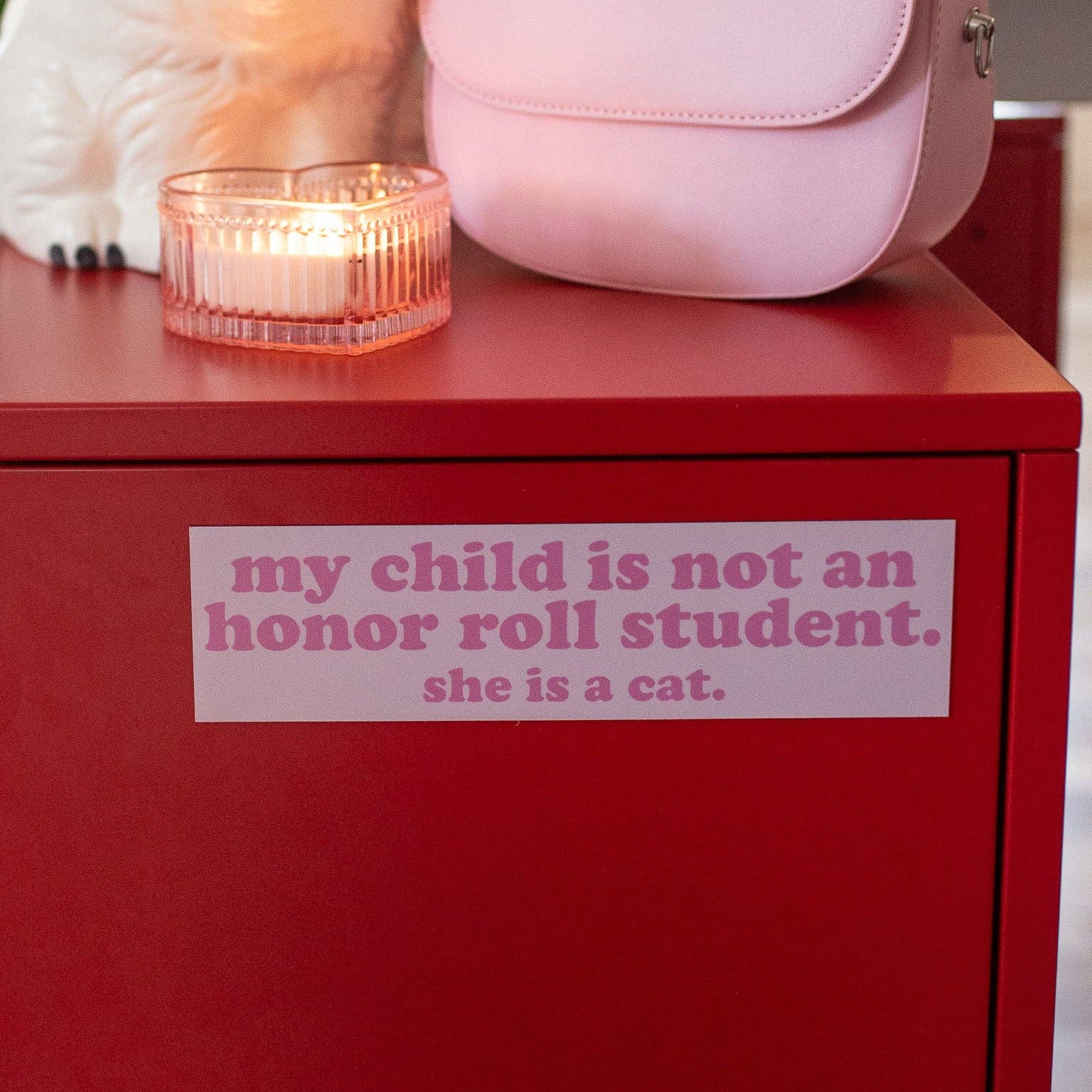 Red cabinet with a pink handbag and candle, featuring a humorous sticker.