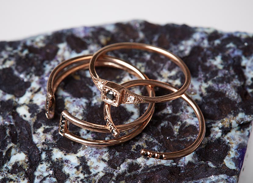 Three rose gold black diamond rings by Jennie Kwon placed on a speckled black and white rock.