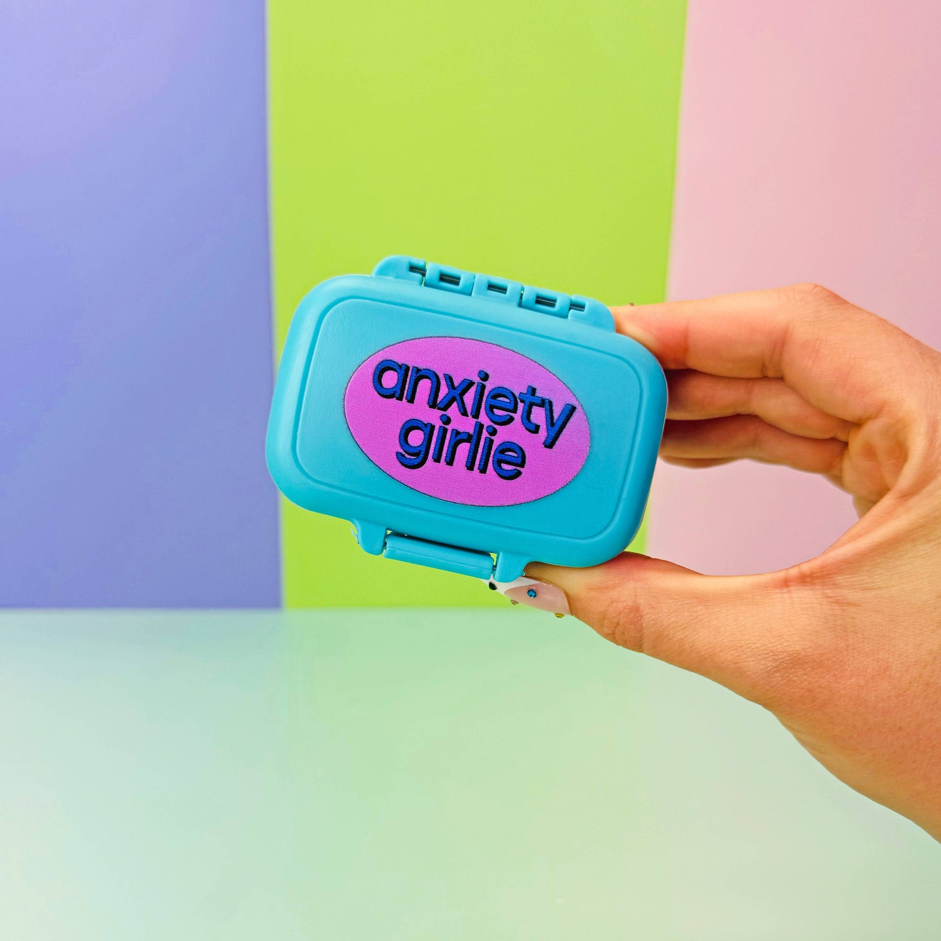 Hand holding a blue 'anxiety girl' container against a colorful background