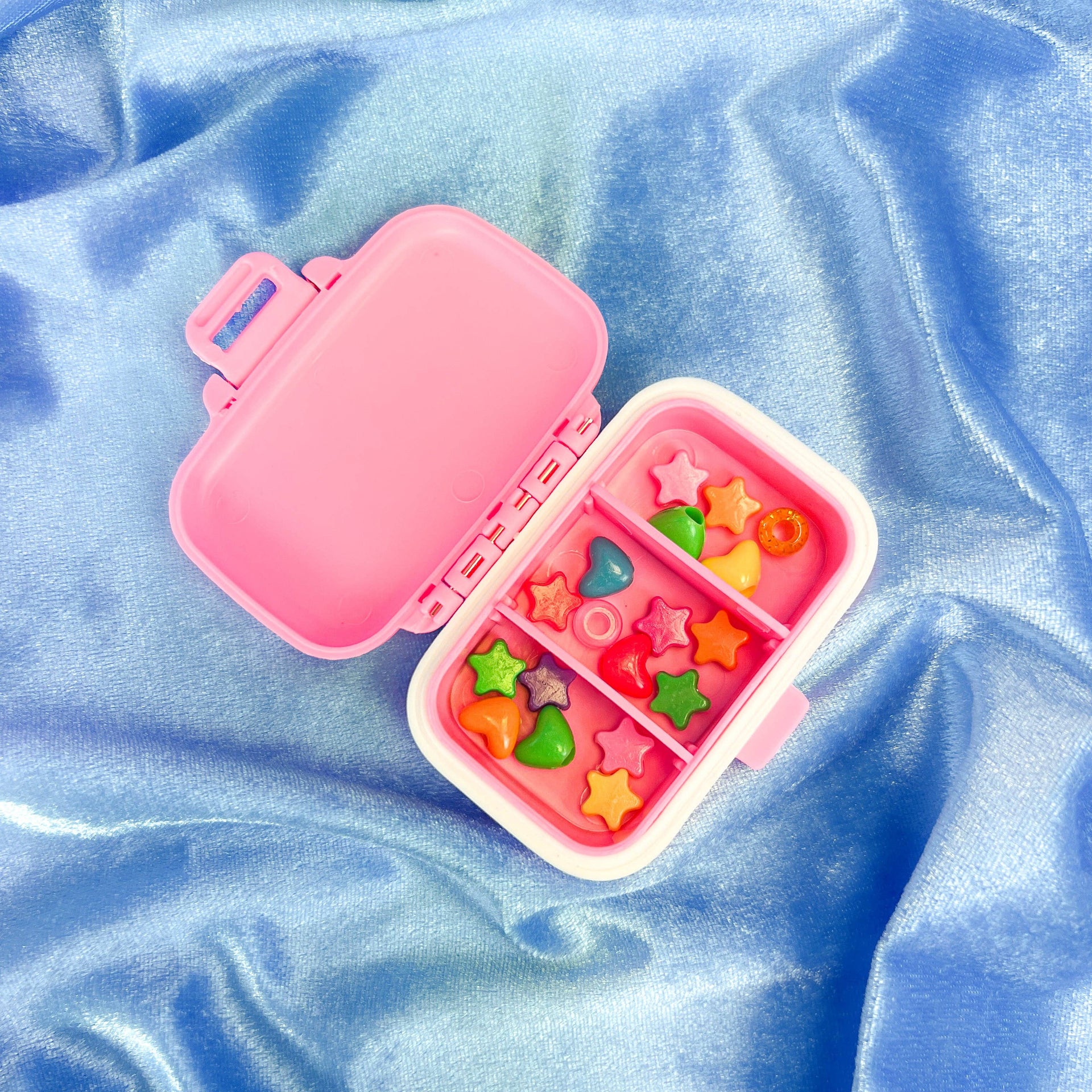 Pink pill box with compartments on a blue fabric background