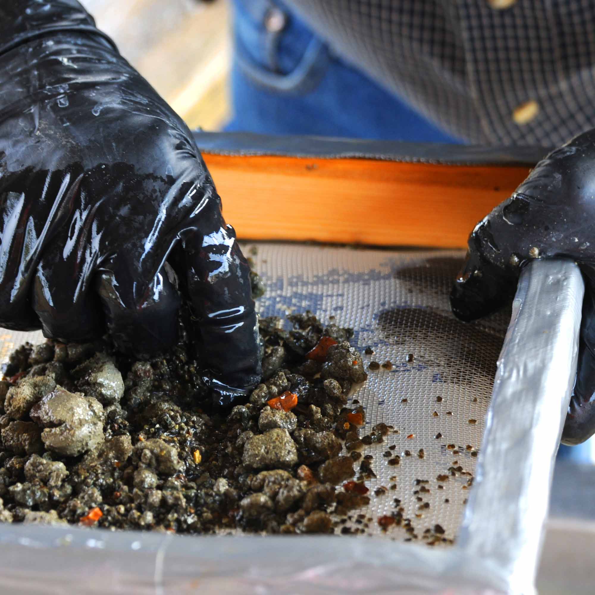 Gloved hands sifting through a trough at an ethical diamond mine.